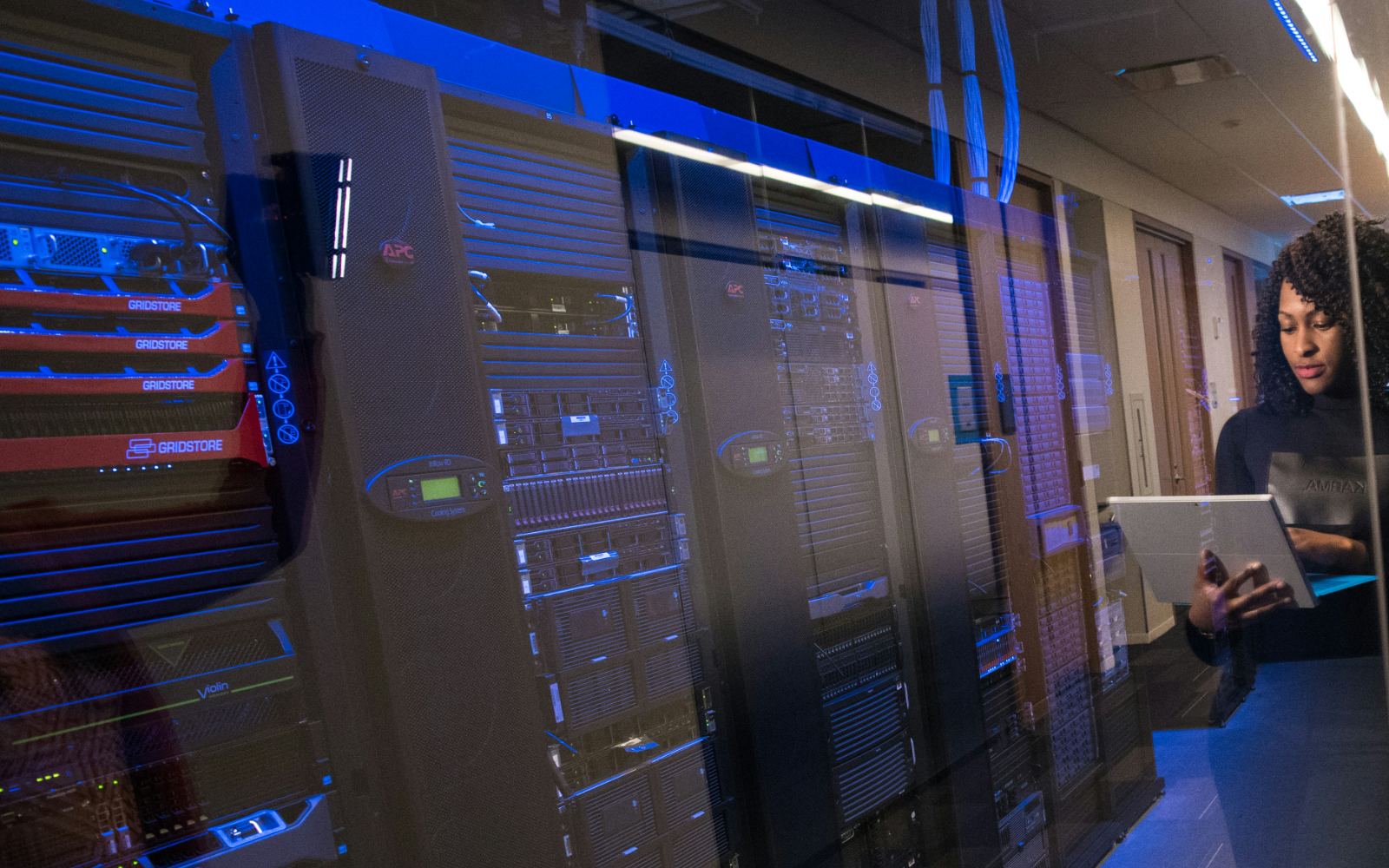 Server racks behind glass in a blue-lit data-centre corridor